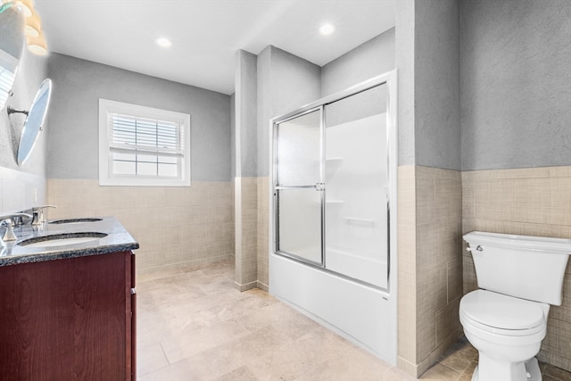 full bathroom featuring bath / shower combo with glass door, vanity, toilet, and tile walls