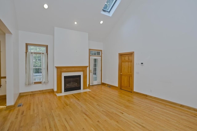 24 High Pines Cir Unit 24, Wilbraham, MA 01095 - unfurnished living room featuring a skylight, high vaulted ceiling, a fireplace with flush hearth, light wood-style flooring, and baseboards