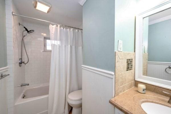 bathroom with toilet, a wainscoted wall, vanity, ornamental molding, and shower / bath combo