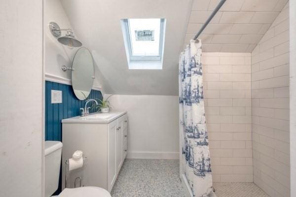 bathroom featuring toilet, lofted ceiling with skylight, tiled shower, and vanity