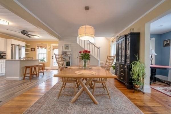 dining area featuring baseboards, a ceiling fan, stairway, ornamental molding, and light wood-type flooring