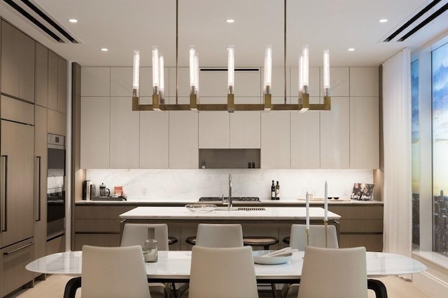 kitchen featuring pendant lighting, stainless steel oven, white cabinets, and a kitchen island with sink