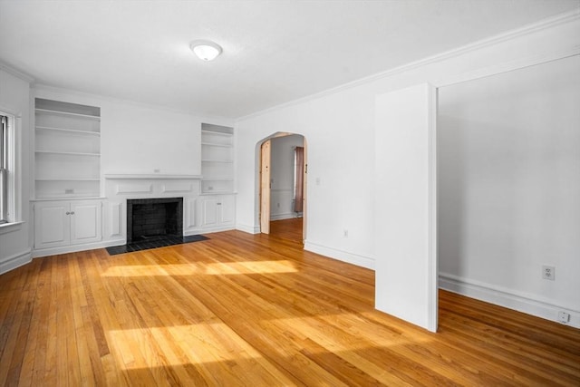 unfurnished living room with built in shelves, ornamental molding, and light hardwood / wood-style floors