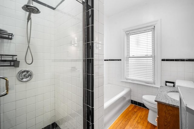 full bathroom with toilet, shower with separate bathtub, tile walls, vanity, and hardwood / wood-style floors