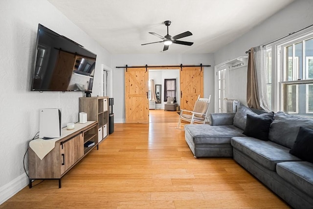 living room with a barn door, ceiling fan, and light hardwood / wood-style flooring