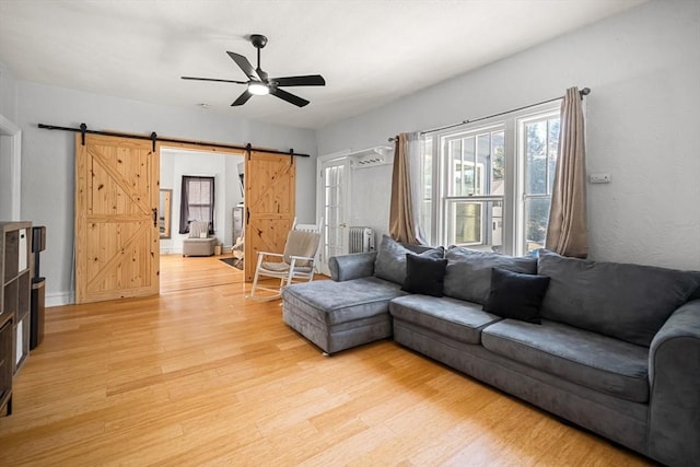 living room with ceiling fan, a barn door, and light hardwood / wood-style floors