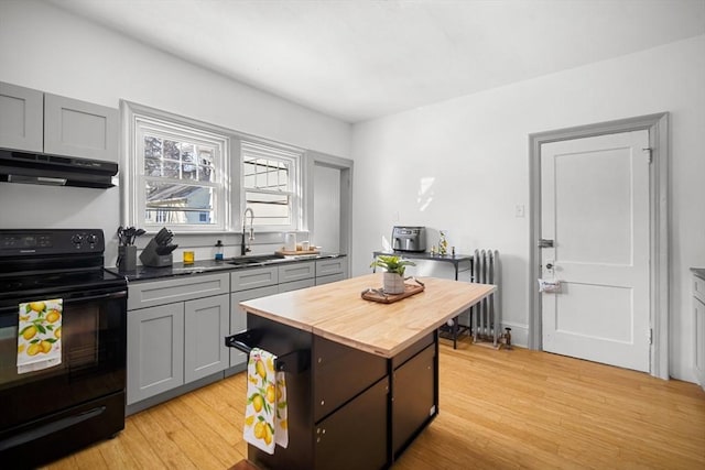 kitchen featuring butcher block countertops, black electric range oven, sink, radiator heating unit, and light wood-type flooring