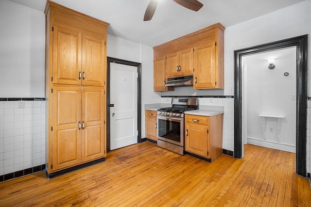 kitchen with tile walls, stainless steel range with gas cooktop, light hardwood / wood-style floors, and ceiling fan