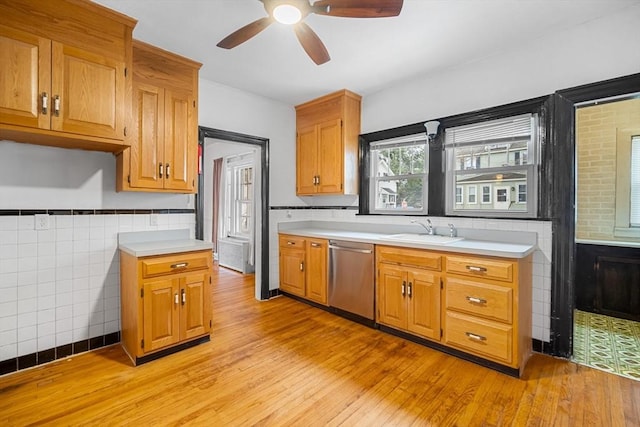 kitchen featuring sink, light hardwood / wood-style flooring, tile walls, stainless steel dishwasher, and ceiling fan