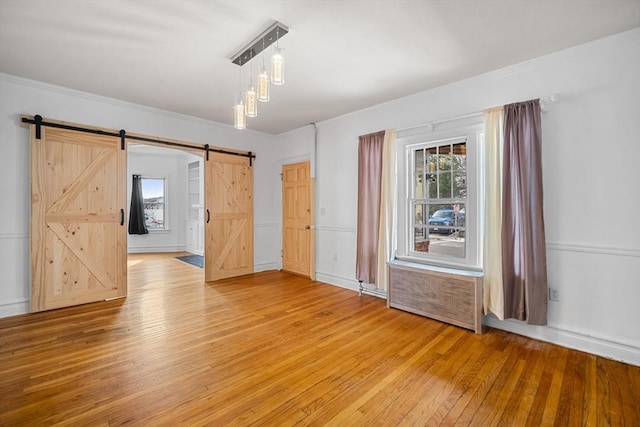 unfurnished room with wood-type flooring, a barn door, radiator heating unit, and crown molding