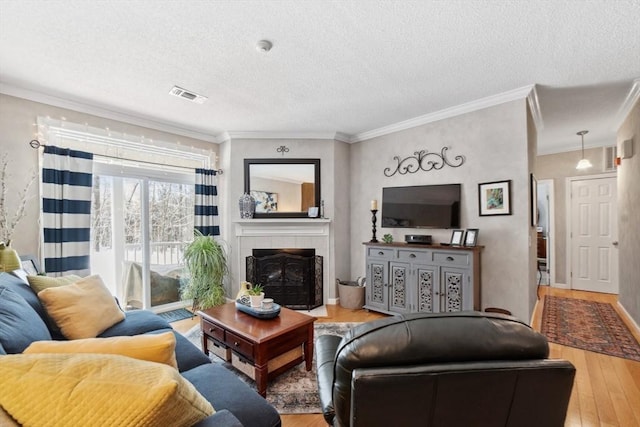 living room with a tiled fireplace, wood-type flooring, ornamental molding, and a textured ceiling