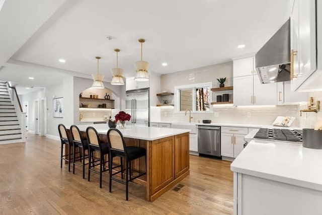 kitchen featuring wall chimney range hood, white cabinets, appliances with stainless steel finishes, light hardwood / wood-style floors, and a center island