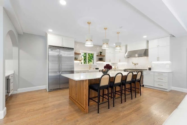 kitchen with high end appliances, a kitchen island, white cabinets, and light hardwood / wood-style floors