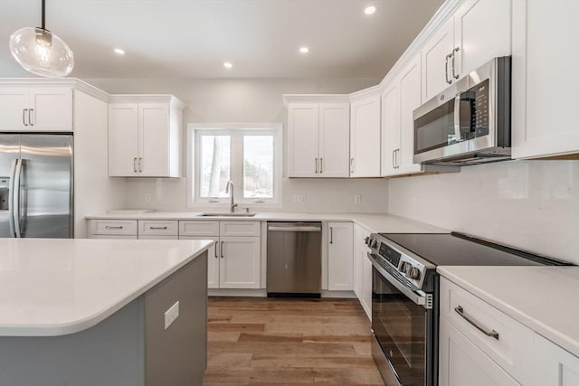 kitchen with sink, white cabinetry, stainless steel appliances, decorative light fixtures, and light wood-type flooring