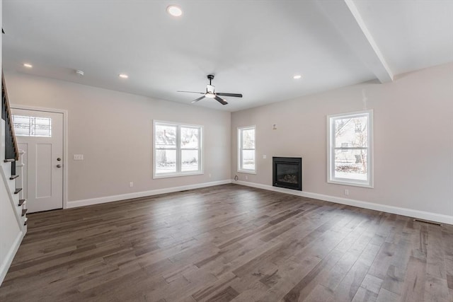 unfurnished living room with beamed ceiling, a wealth of natural light, dark hardwood / wood-style floors, and ceiling fan