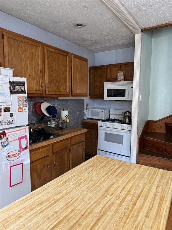 194 Fells Ave, Medford, MA 02155 - kitchen featuring white appliances, brown cabinets, tasteful backsplash, a textured ceiling, and butcher block counters