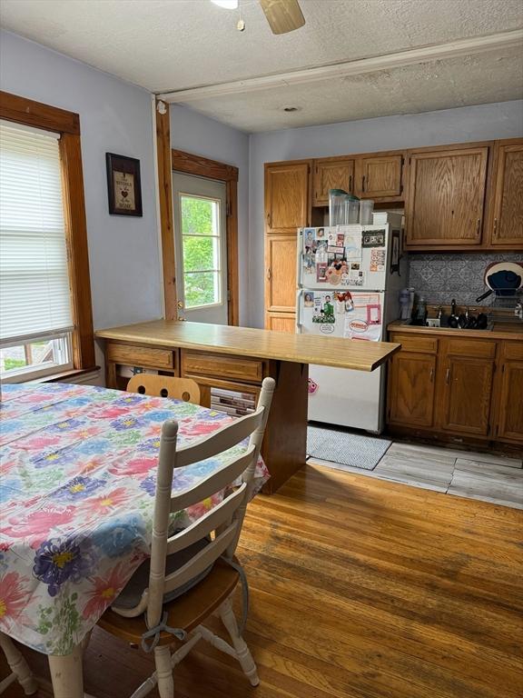194 Fells Ave, Medford, MA 02155 - kitchen with freestanding refrigerator, brown cabinetry, light wood finished floors, a sink, and a textured ceiling