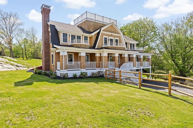 view of front of property featuring a chimney, a front yard, covered porch, and roof with shingles