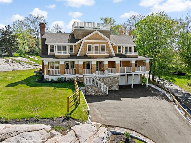 back of property featuring an attached garage, driveway, a porch, a balcony, and a yard