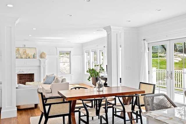 dining area with french doors, healthy amount of natural light, light wood-style floors, ornamental molding, and a fireplace