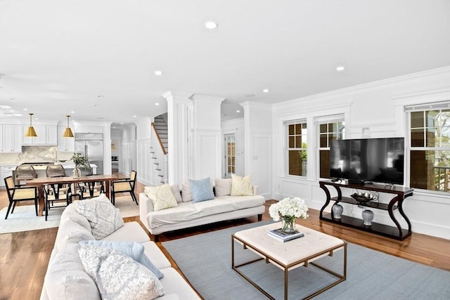 living area featuring stairs, wood finished floors, ornamental molding, a decorative wall, and recessed lighting