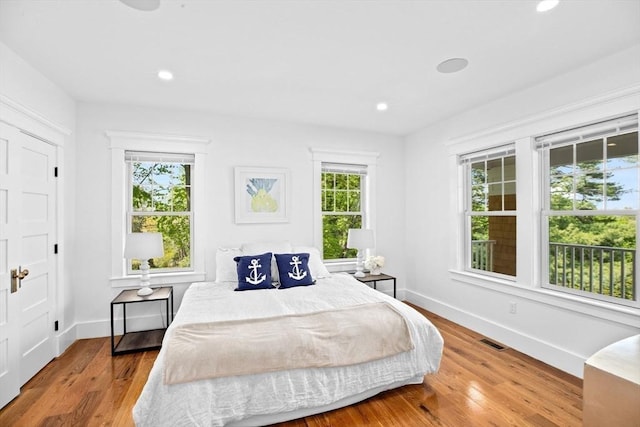 bedroom with multiple windows, wood finished floors, baseboards, and recessed lighting