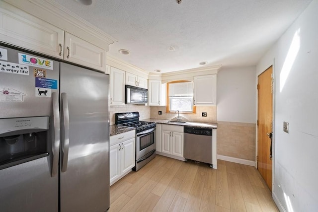 kitchen with a wainscoted wall, stainless steel appliances, light wood-style flooring, white cabinets, and a sink