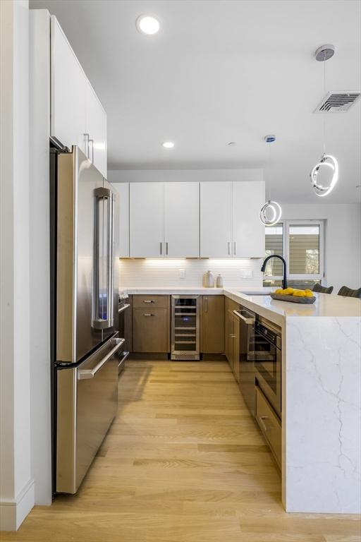 kitchen with white cabinets, hanging light fixtures, wine cooler, appliances with stainless steel finishes, and light hardwood / wood-style floors