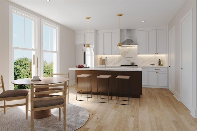 kitchen featuring wall chimney exhaust hood, white cabinetry, and an island with sink