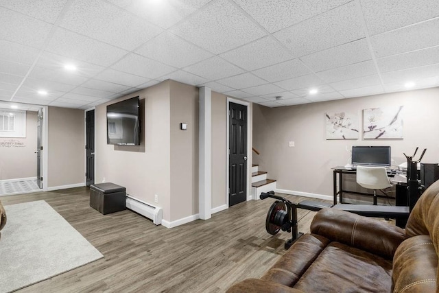 living room featuring a drop ceiling, a baseboard heating unit, and wood-type flooring