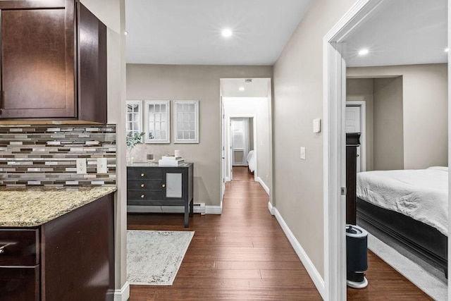 kitchen featuring dark brown cabinets, dark wood-type flooring, decorative backsplash, and light stone counters