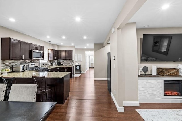 kitchen with light stone countertops, appliances with stainless steel finishes, hanging light fixtures, a kitchen breakfast bar, and backsplash