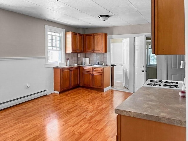 kitchen with light hardwood / wood-style floors, gas stovetop, a baseboard heating unit, decorative backsplash, and sink