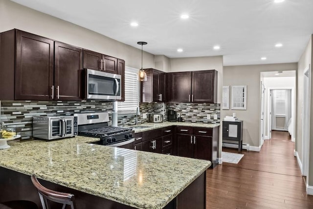 kitchen featuring light stone countertops, a baseboard radiator, decorative light fixtures, stainless steel appliances, and kitchen peninsula