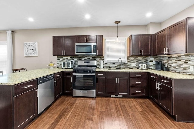 kitchen with kitchen peninsula, dark hardwood / wood-style flooring, sink, decorative light fixtures, and stainless steel appliances