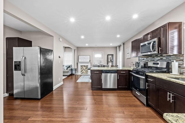 kitchen with kitchen peninsula, dark hardwood / wood-style flooring, backsplash, light stone countertops, and stainless steel appliances