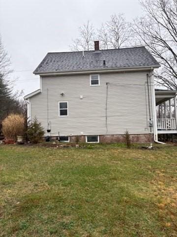 rear view of house featuring roof with shingles, a chimney, and a lawn