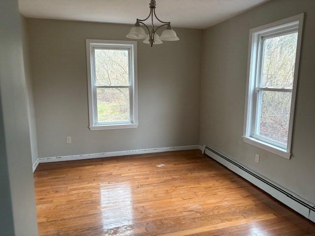 empty room featuring light wood finished floors, baseboard heating, baseboards, and an inviting chandelier