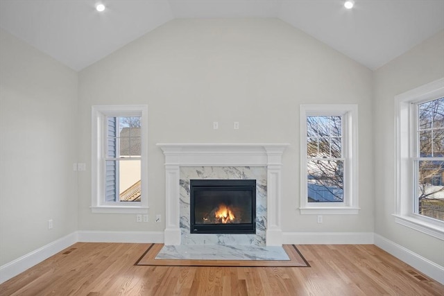 unfurnished living room with a wealth of natural light, a premium fireplace, lofted ceiling, and light wood-type flooring