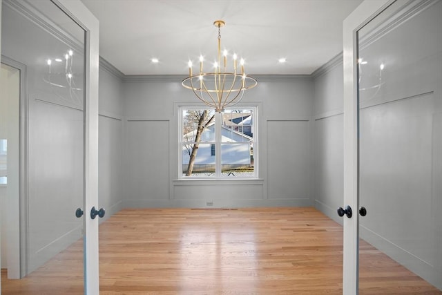 unfurnished dining area with crown molding, french doors, light hardwood / wood-style flooring, and an inviting chandelier