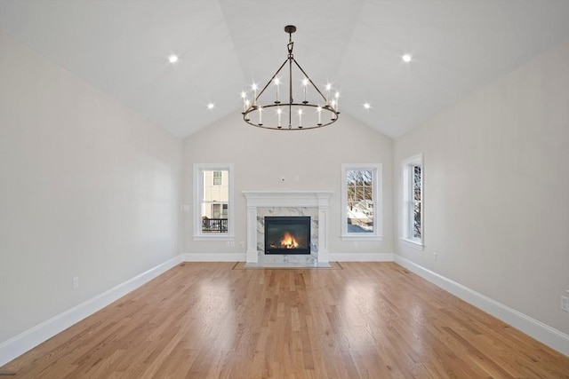 unfurnished living room featuring a notable chandelier, high vaulted ceiling, a high end fireplace, and light hardwood / wood-style flooring