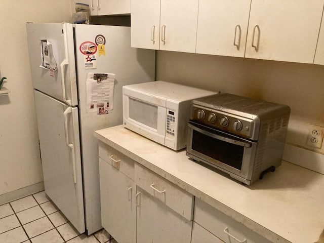 kitchen with white appliances, white cabinets, and light tile patterned flooring