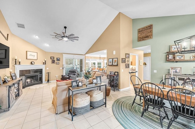 tiled living room with ceiling fan, a tile fireplace, and high vaulted ceiling