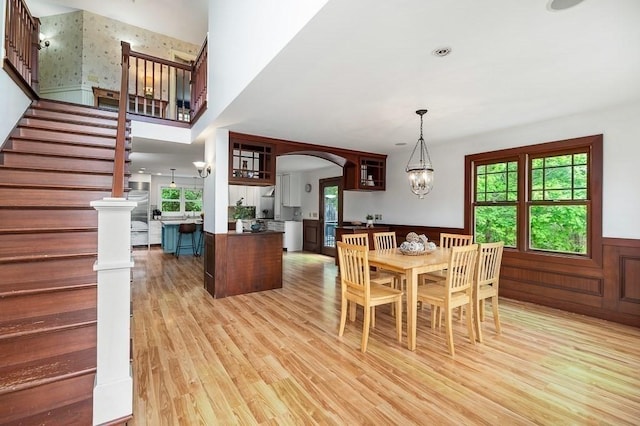 32 Witham St Unit B, Gloucester, MA 01930 - dining space with wainscoting, light wood finished floors, arched walkways, stairs, and a chandelier