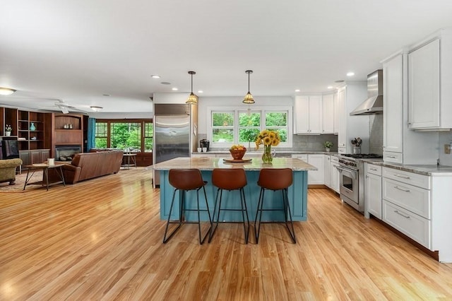 32 Witham St Unit B, Gloucester, MA 01930 - kitchen with high end appliances, wall chimney range hood, white cabinets, open floor plan, and light wood finished floors
