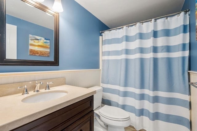 bathroom featuring vanity, toilet, curtained shower, and a wainscoted wall