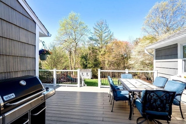 wooden deck featuring outdoor dining area, an outbuilding, grilling area, and a storage shed