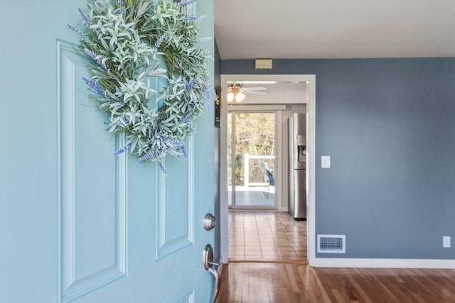 foyer with baseboards, a ceiling fan, wood finished floors, and visible vents