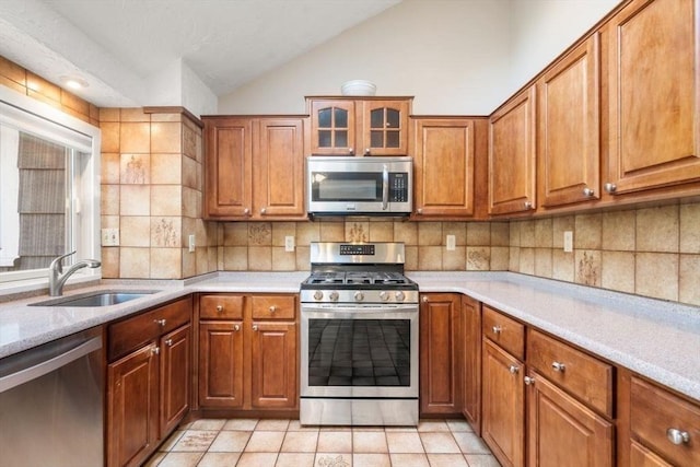 kitchen featuring a sink, light countertops, brown cabinetry, stainless steel appliances, and vaulted ceiling