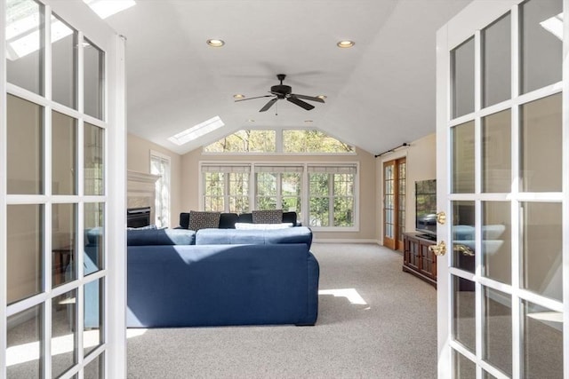 carpeted living room with ceiling fan, a fireplace, french doors, recessed lighting, and lofted ceiling with skylight